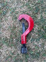 Photo of the tubing cutter lying on grass showing front side with cutting wheel and lever.