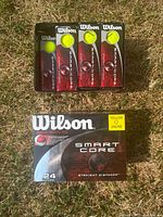 Top-down photo of Wilson Smart Core Yellow golf balls in black tubes with yellow balls visible, inside an open box on grass.