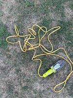 Yellow work light with metal cage and built-in outlet, attached to a long yellow extension cord laying on grass.