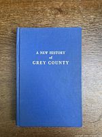 Front cover of a blue hardcover book titled A New History of Grey County shown on wooden surface.