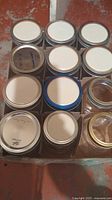 Carton holding 12 small clear glass Mason jars with metal screw bands and used lids