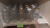 Shelf with approximately 27 clear Mason jars