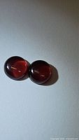 Photo showing two round garnet cabochon gemstones with deep red translucent appearance, polished domed shape.
