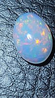 Close-up photo of the natural Ethiopian oval opal cabochon showing multicolored play of colors on a dark textured background.