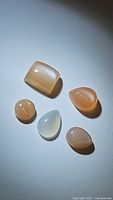 Five polished moonstones in different shapes and colors displayed together under focused light showing cat's eye effect.