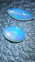 Pair of natural Ethiopian opals showing multicolored play of color on black textured surface. One marquis cut and one oval cabochon cut visible.