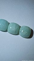 Three natural amazonite cushion cabochons arranged side by side on a light surface, showing texture and pale green colors.