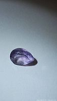 Close-up photo of pear cut natural purple pink amethyst gemstone showing facets and color.