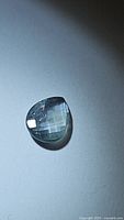 Photo of the aqua blue sapphire gemstone showing the pear shape and checkerboard cut under directional lighting.