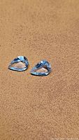 Two natural pear shaped aquamarine gemstones displayed on a brown textured surface, showing color and cut of stones.