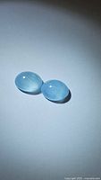 Pair of natural lagoon blue aquamarine oval cabochon gemstones on white background showing their smooth translucent glossy surface and natural inclusions.