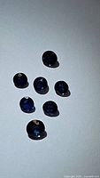 Seven natural blue sapphires of varying sizes and rich royal blue color displayed on a light surface.