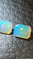 Close up of two natural Ethiopian opals, showing translucency and multicolored flashes on textured dark surface.