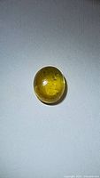 Oval natural deep golden yellow sapphire cabochon with visible inclusions.