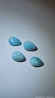 Four pear-shaped Larimar cabochons displayed on a flat surface with bright lighting highlighting the blue and white color matrix.