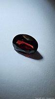 Oval natural garnet gemstone with deep cherry red color, faceted and laid on grey surface showing reflection and light play.