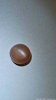 Photo of the natural peach moonstone oval cabochon gemstone showing the cat's eye effect under lighting.