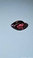 Faceted pear cut pink tourmaline gemstone lying flat showing the depth and facets of the stone under direct light.