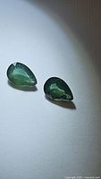 Pair of pear cut green sapphires on white background showing color and cut from one angle