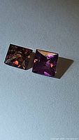 Pair of princess cut squared sapphires laid side by side, showing brown and purple colors on a neutral background