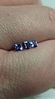 Three cushion cut tanzanite gemstones placed on skin to show scale and clarity, displaying their blue to violet coloration and flawless quality.