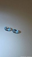 Two oval cut natural sky blue topaz gemstones placed on white background showing color and cut.