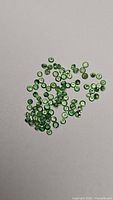 Photo of round cut natural Tsavorite garnet stones in various sizes, green color, spread on a white background.