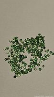 Pile of tiny green tsavorite garnet stones on plain background, showing color and cut detail