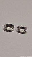 Two oval cut light color morganite gemstones with good clarity, placed on a white surface.