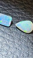 Two faceted natural untreated Ethiopian opal gemstones on textured black surface. One emerald cut rectangular shape and one pear shaped opal with multicolored flashes visible.
