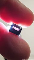 Close-up photo of a deep dark purple octagon cut tourmaline held between fingers with backlight showing internal clarity and color depth.