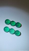 Six round vivid green onyx cabochons arranged in two rows of three on light background, showing glossy polished rounded surface and transparency.