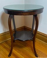 Full view of walnut occasional table showing round glass top, legs, and lower shelf