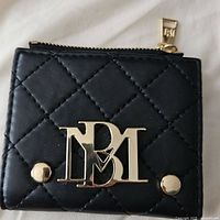 Close-up of black quilted bifold wallet front with gold-tone Badgley Mischka logo and button studs.
