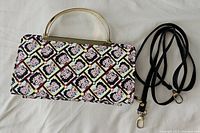 Front view of Betty Boop clutch purse with metal frame handle and black detachable strap laid beside it.