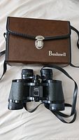 Bushnell binoculars with case on white surface showing overall lot contents and carrying case details.