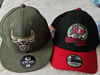 Two sports hats side by side: green Chicago Bulls, black and red Buccaneers on white background