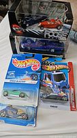 Photo showing two boxed Foose car sets and several Hot Wheels cars in package arranged on a white surface