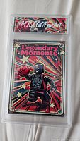 Front of the card titled Legendary Moments showing LEGO style basketball player in Chicago Bulls number 23 jersey with a red, black and gold starburst background encased in a hard protective plastic sleeve with signature label.