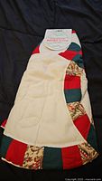 Quilted Christmas tree skirt with tag labeled 'Holiday Classics'. Visible cream center and red, green, and patterned border in folded position.