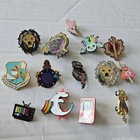 Full display of 14 assorted enamel pins arranged on a light fabric surface.