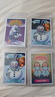 Four Garbage Pail Kids cards: Winning Shisa, Jack Frost, Twin Tara, and an unidentified card, displayed in plastic sleeves on a light surface.