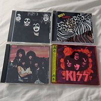 Four KISS CDs arranged on a white surface showing album covers with makeup faces and animal print backgrounds