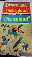 Cover of Disneyland magazine showing Mickey Mouse, Goofy, and Donald Duck climbing and hiking on a mountain with playful background