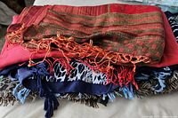 Five vintage shawls stacked, showing colors, fringe details, and woven patterns.