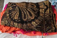 Close-up photo showing a folded shawl with dark background and gold paisley and floral patterns