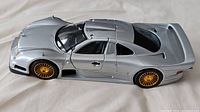 Side view of the silver Maisto Mercedes Benz CLK-GTR model showing gold spoke wheels and aerodynamic body shape.