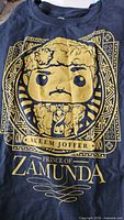 Photo showing front graphic of black T-shirt with Funko Pop character Akeem Joffer, Prince of Zamunda in gold print.
