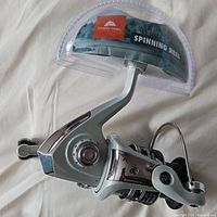 Front angle view of the spinning reel showing its silver and chrome body, ergonomic handle, and part of the clear packaging.