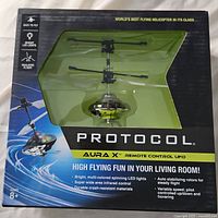 Front box view of Protocol Aura X remote control UFO helicopter in green and black, showing product and packaging with features listed.